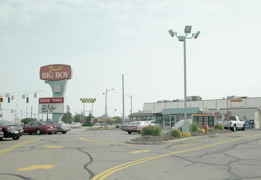 Carpark of an American diner with a few cars in spaces, cracked tarmac and yellow road markings