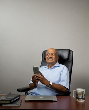 App inventor Ramesh Jain sits at his desk holding his smartphone and smiles off into the distance