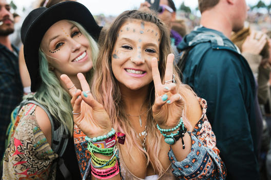 two hippie girls flashing peace signs in the middle of a crowd