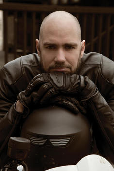 A motorcycle rider with leather gloves sitting on his motorcycle and resting face on hand