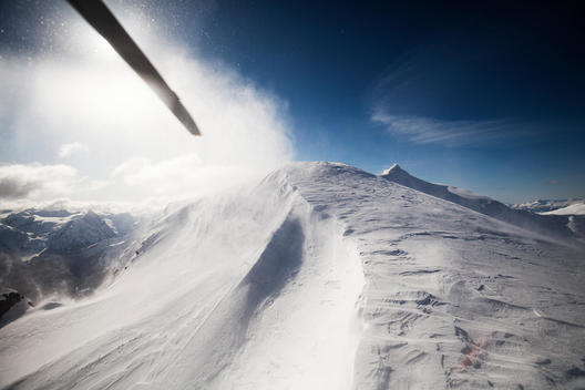 Aerial perspective of snowy peak landing zone with helicopter blade swirling.