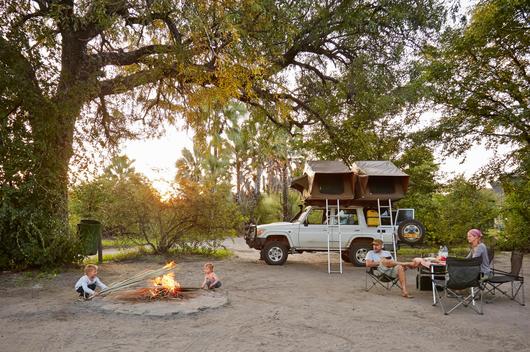 Off road vehicle parked, family relaxing around camp fire, Nata, Makgadikgadi, Botswana