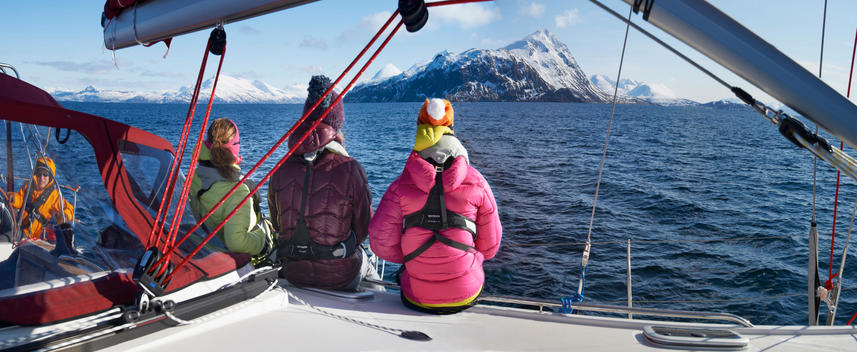 Three women sitting on sailing yacht on fjord with snowy mountains in the background