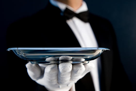 Close up of a waiter wearing white gloves holding a silver tray in his hand