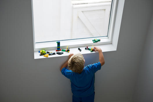 Young boy in blue tee shirt playing with building bricks on a windowsill
