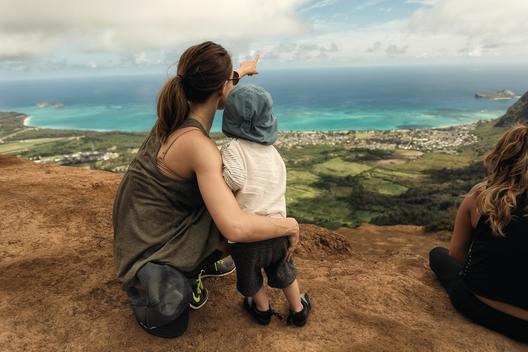 Mother and child looking at view of ocean and valley from top of mountain