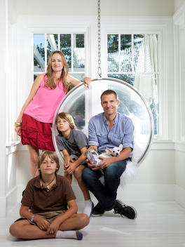 Dad, son, and dog are sitting in a round chair with mom standing and other son sitting on the floor