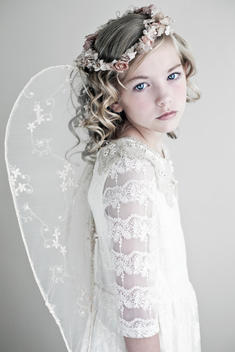 Female youth with blonde hair and blue eyes wearing lace dress and angels wings with frown of small flowers