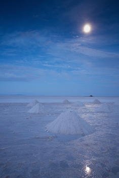 Salt cones in the moonlight, with moon reflected in salt water; Salar de Uyuni, Bolivia