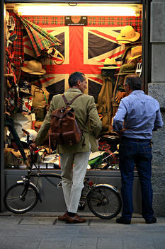 Two men, one with a bicycle, chatting outside a hunting equipment showcase, with a Great Britain\'s flag on the background.