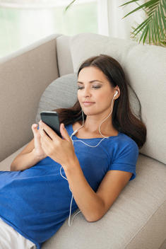 Young woman reclining on sofa listening to music on smartphone