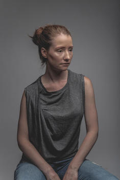 androgynous female, with red hair pulled back. Wearing grey t-shirt with sleeves rolled up. Looking away from camera.