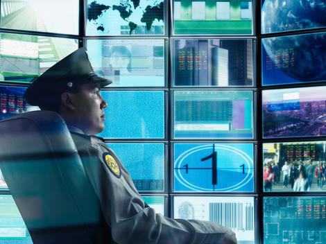 Male security guard sitting in front of monitor screens