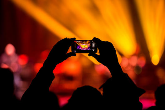 A person holding up an android phone taking pictures at a concert.