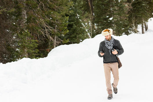 Man checking cell phone while walking down snow packed road on brisk wintery day
