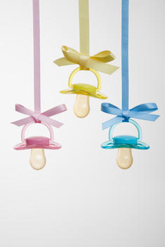 Baby pacifiers hanging from ribbons against a plain background.