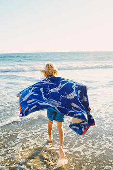 a boy running in the sea using a beach towel as a wings