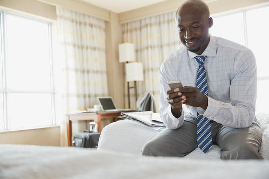 Smiling businessman using smart phone in hotel room
