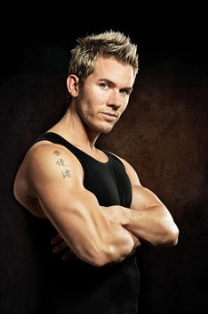 Portrait of athletic caucasian male with arms crossed on dark background.
