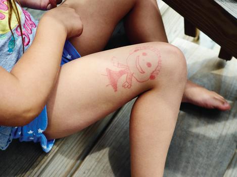 Girl in shorts sitting on porch stairs with drawing on leg.