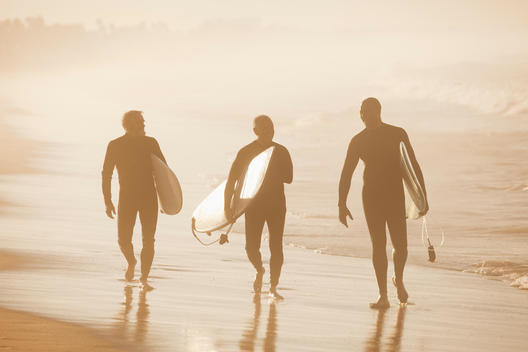 Older surfers carrying board on beach