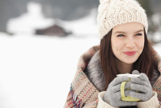 Close up of smiling woman in knit hat and gloves drinking coffee in snowy field