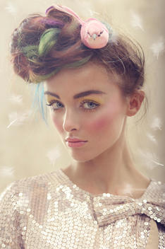 Beauty shot of a young caucasian girl, wearing a sequin top, hair up with a bird sitting on her multicolor bun. Looking in the lens