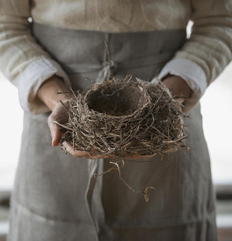 An organic farm in winter in New York State, USA. A woman in a work apron holding a woven twig bird nest.