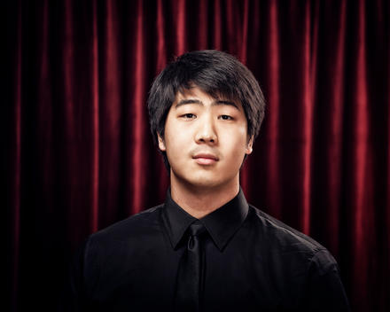 young adult man wearing black in front of red stage curtain