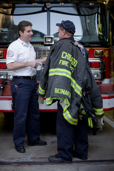 Two Chicago Firefighters Stand In The Fire Department Garage.