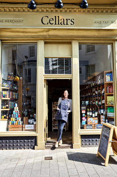 A small business owner stands happily in the doorway of her wine store