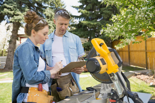 Couple with clipboard at table saw in backyard