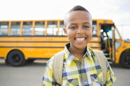Portrait of happy little boy against school bus
