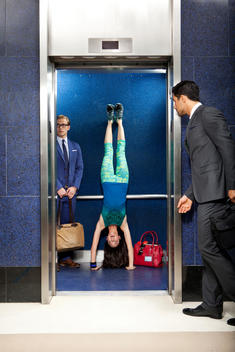 A young woman does a handstand inside an elevator next to a businessman