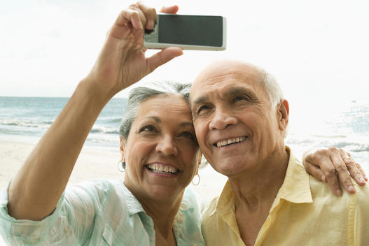 Older Hispanic couple taking selfie on beach