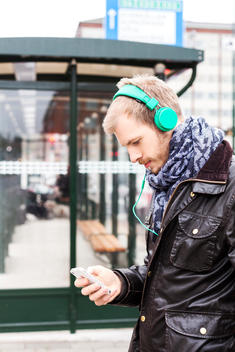 Side view of man listening music through mobile phone while waiting at bus stop