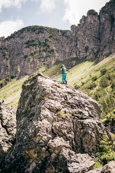 6 year old boy in blue pants climbing large boulder in alpine landscape.