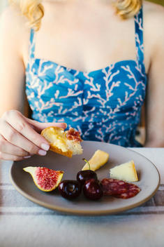 Woman in blue coral print dress with plate of food including cheese, bread and figs