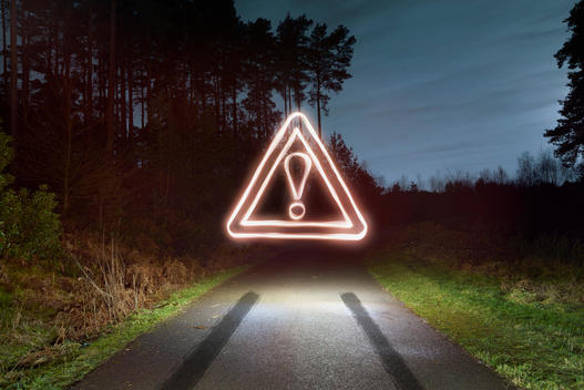 Tyre skid marks and glowing road warning sign above forest road at night