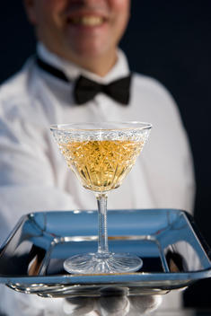 Close up of a smiling waiter wearing white gloves offering a drink on silver tray