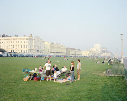 Groups of people having picnics on Hove Lawns near Brighton beach on a summer\'s evening. Regency houses overlooking the seafront can be seen in the distance.