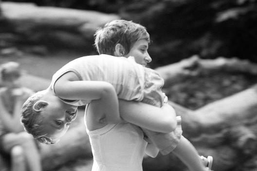 A young mother playfully carries her smiling son over her shoulder as she runs through the wood at the Donald and Barbara Zucker Natural Exploration for children at Prospect Park, Brooklyn, NYC