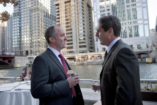 Two Business Men Talk At An Outdoor Patio Next To The Chicago River.