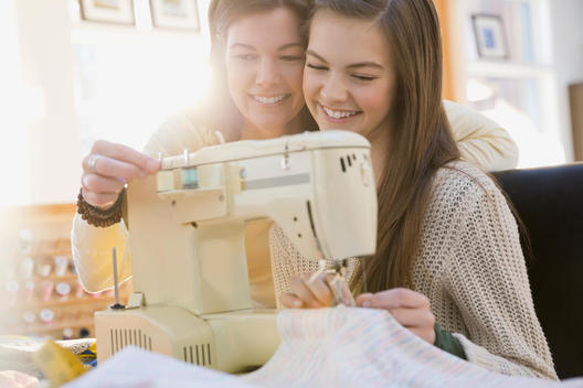 Mother teaching daughter how to use sewing machine