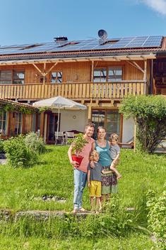 Portrait of young family, holding pot plant, standing in front of house with solar panelled roof