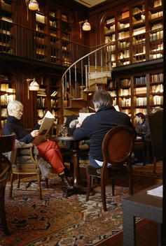 People sitting at tables and reading in the library of the Nomad hotel