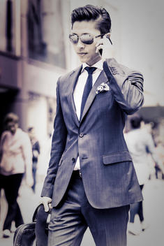 asian businessman with leather bag and sunglasses walking by and talking on the phone