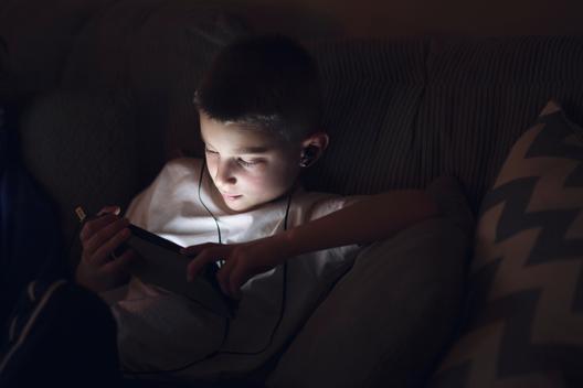 Boy on sofa wearing earphones looking down using digital tablet