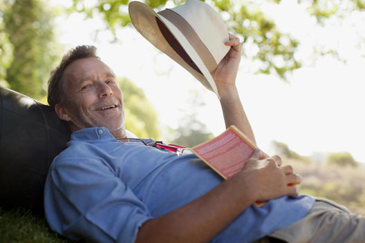 Portrait of smiling man laying on grass with book and hat
