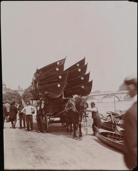 Horse-Drawn Wagon With Attending Men Carrying Eight Boats Alongside The Thames River.